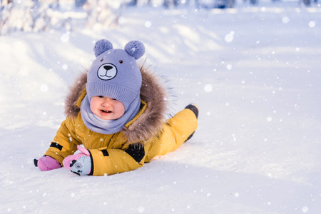Toddler 12-17 months old in yellow winter clothes slipped and cries while walking in a winter parkの写真素材