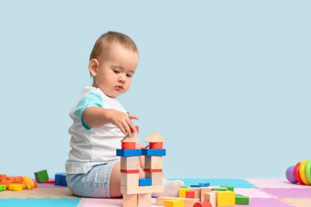 Toddler 12-17 months old builds a tower of wooden cubes sitting on the floor in the playroomの写真素材