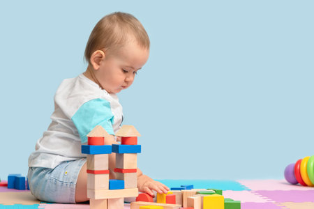 Toddler 12-17 months playing with a designer of colorful wooden cubes sitting on the floor in the playroom. copy spaceの写真素材