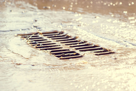 The grate of the storm sewer after the rain. The water drains into the storm drain. Selective focus, defocused backgroundの写真素材