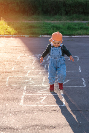 A 2-year-old child jumps on hopscotch at sunsetの写真素材