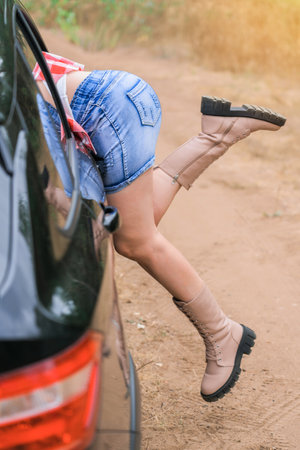 Women's legs stick out of the car window, a woman climbs into the car through an open windowの写真素材