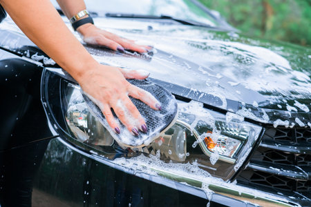 A woman's hand with a sponge washes the headlight of a car, close-upの写真素材