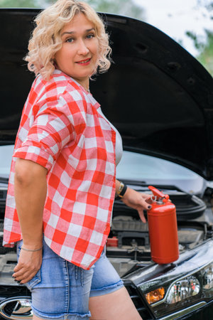a middle-aged woman with a fire extinguisher in her hands poses standing by the open hood of a carの写真素材