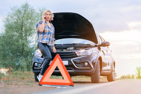 A woman calls the service department standing at the open hood of the car, an emergency stop signの写真素材