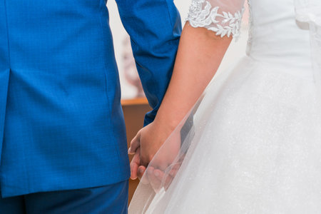 The newlyweds are holding hands. A man in a blue suit holds a woman in a white wedding dress by the hand. close-up.の写真素材