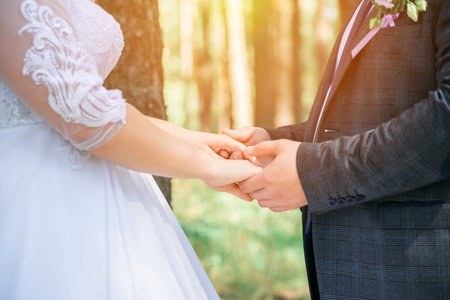 The newlyweds in the forest hold each other's hands in the sunlight.の写真素材
