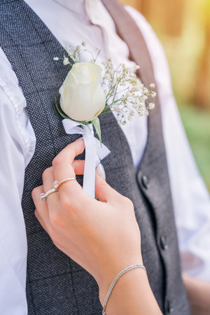 A woman's hand adjusts the boutonniere on the groom's vest.の写真素材