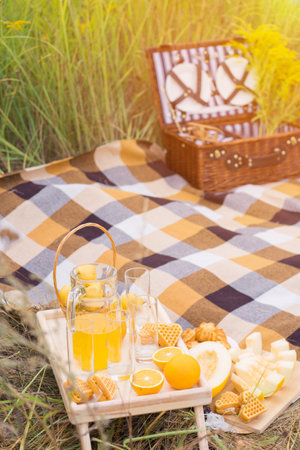 A basket and a table with fruits and pastries at a picnic in summer, in the rays of sunset light.の写真素材