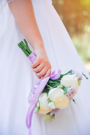 A bride in a wedding dress holds a bouquet of white roses and lilac carnations.の写真素材