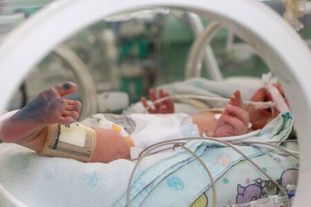 Incubator with a sick newborn baby at neonatal intensive care unit. feet with ink from footprintの写真素材