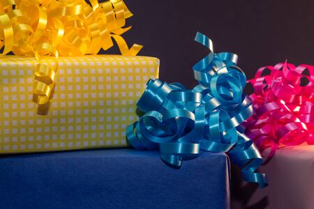A yellow, blue and pink present with bows close up, partial view, with a dark blue background. Celebration conceptの写真素材