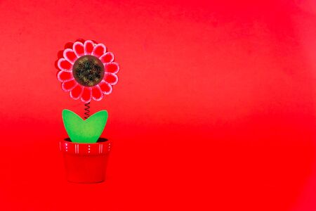 One isolated handmade wooden flower and green double leave in a small red planter on a red background standing straight. woman, unique and happy concept, mother day.の写真素材