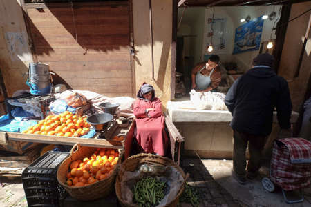 Old man selling fruits and vegetables in the roadside market Souk in the city of Fes in Morocco. Local shops on the road. A seafood shop next to a fruits shop.のeditorial素材