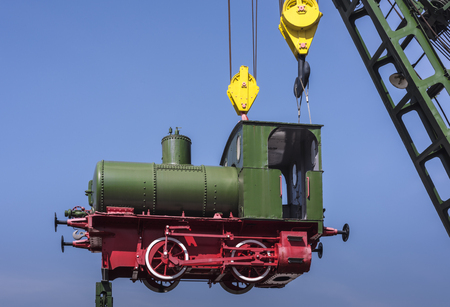 Cute little green nostalgic steam train hanging in the air on a crane truck, blue skies and copy...