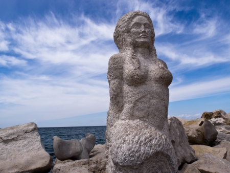 A mermaid sculpture carved from stone A rocky background the sea and the Blue Sky, town of Piran in Sloveniaの写真素材