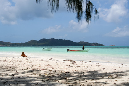 Tropical beach biew, with blonde woman sitting in the sun, and fishermanのeditorial素材