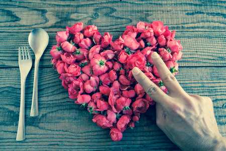 Heart made of red roses in wooden background, covered by an hand to represent personal feelings, denin vintage effectの写真素材
