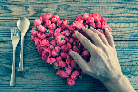 Heart made of red roses in wooden background, covered by an hand to represent personal feelings, denin vintage effectの写真素材