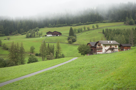 ST. MAGDALENA, ITALY - SEPTEMBER 14, 2015: Traditional houses in a cloudy mornig surrounded by green pasture next to the little town of St. Magdalena in Val di Funes, no people aroundのeditorial素材