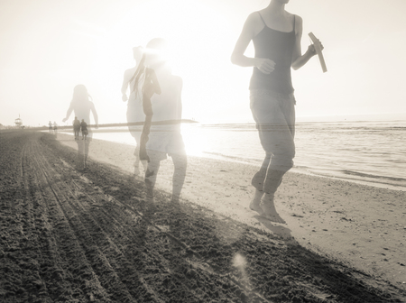 Mother and daughter next to the other running long the shoreline of an Italian beach in the early morningの写真素材