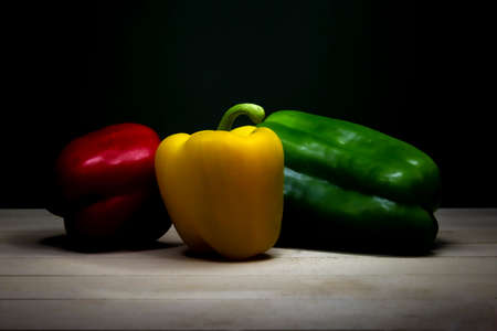 Peppers on a wooden table. Low-key still-life photo of red, yellow and green peppers, made on studio with black background and softboxの写真素材