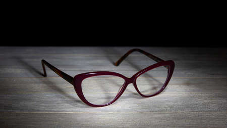Eyeglasses on a wooden table. Low-key still-life photo, made on studio with black background and softboxの写真素材