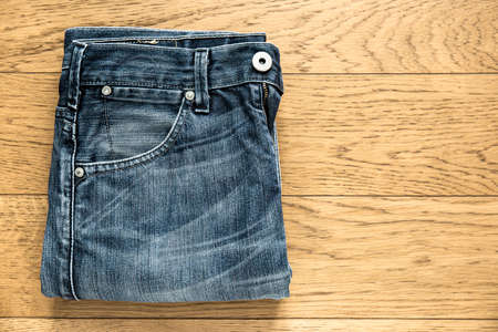 Denim jeans folded on wooden table. Close-up picture taken in studio representing a pair of jeans on a wooden floor.の写真素材
