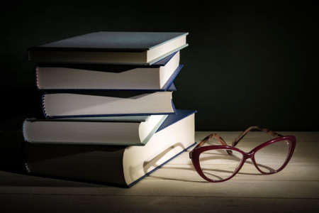 Stack of books with eye-glasses on a table. Low-key still-life photo, made on studio with black...