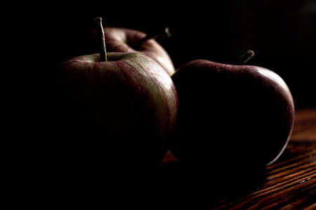 Apples in the dark. Low-key picture of three apples on a wooden table. Still-life studio shot.の写真素材