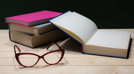 Stack of books with eye-glasses on a table. Low-key still-life photo, made on studio with black...