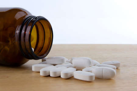 White pills spilled on the table from a container. Close up picture taken in studio with softbox.の写真素材