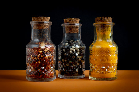 Spices in glass jars. Hot pepper, black pepper and turmeric powder in containers closed with corks.の写真素材