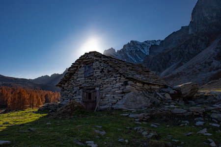 Mountain cabin at dawn. Autumn landscape with a traditional alpine stone building in backlight and orange larches in the background. Picture taken at Alpe Devero (Italy).の写真素材