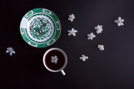 cup of black tea, a saucer with an image of a dragon, white flowers on a dark backgroundの写真素材