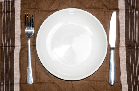 Blank plate with fork and knife on tablecloth backgroundの写真素材