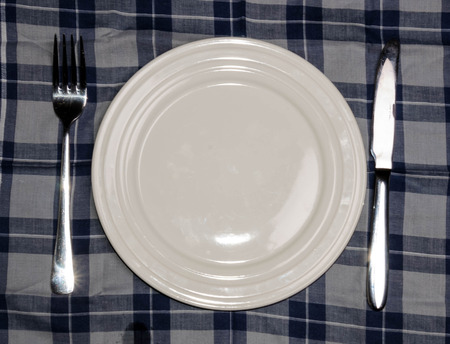 Blank plate with fork and knife on tablecloth backgroundの写真素材