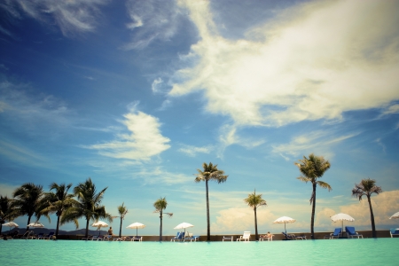 Beach with palm trees and sun loungers on the background of blue skyの写真素材