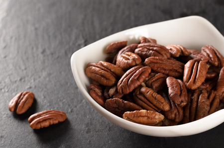 Triangular bowl full of tasty peeled pecan nuts on a black slate plate, selective focus