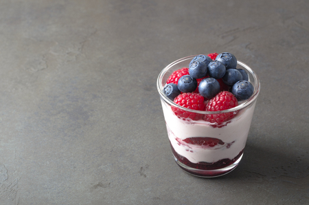 Glass of homemade yogurt with fresh blueberries and raspberries. Gray background, copy spaceの写真素材