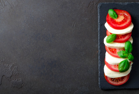 Traditional italian food, sliced tomatoes and mozzarella on a slate plate, dark stone background. Top view, copyspaceの写真素材