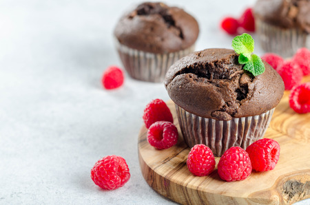 Three chocolate muffins on a wooden board with fresh raspberries and mint leaf, copy space for your textの写真素材