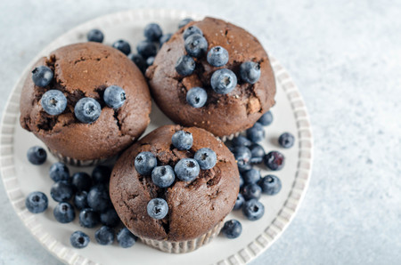 Three homemade chocolate muffins with fresh blueberries on a white plate, horizontal image, top viewの写真素材