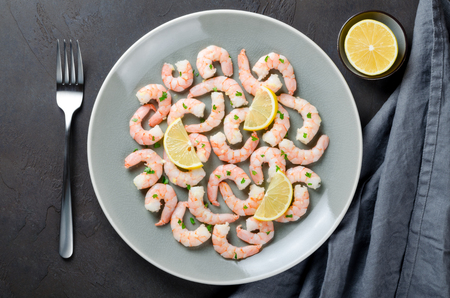 Gray plate full of peeled roasted prawns made with garlic and ginger sauce, served with lemon slices on a dark stone background. top viewの写真素材