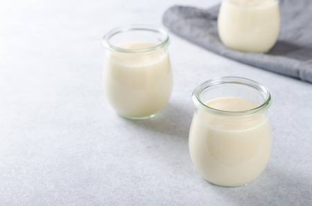 Three glass jars with lemon or vanilla curd dessert on a light stone tableの写真素材