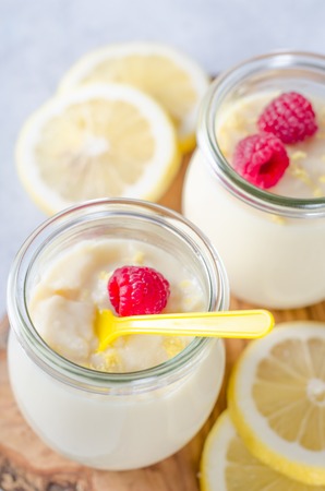 Two glass jars with lemon or vanilla dessert with raspberries and lemon slices on a wooden board, vertical imageの写真素材
