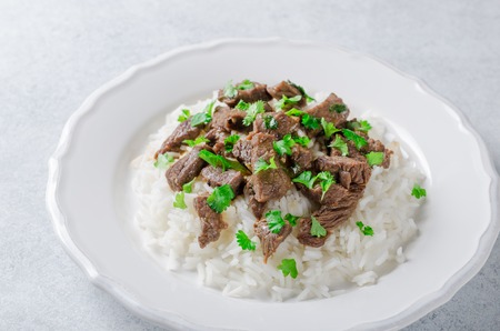 A white plate with rice and fried beef in a sauce with parsleyの写真素材