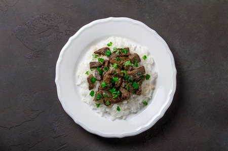 A white plate with rice and fried beef in a sauce with parsleyの写真素材