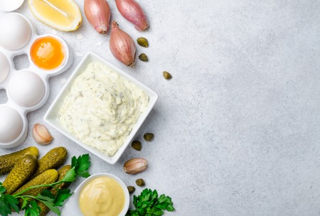 Homemade traditional french sauce remoulade in a white bowl with ingredients, lemon, eggs, shallot...