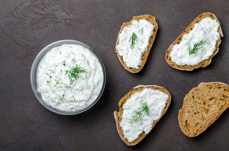 Homemade greek tzatziki sauce in a glass bowl with sliced bread on a dark black stone background. Top view, horizontal image, copy spaceの写真素材